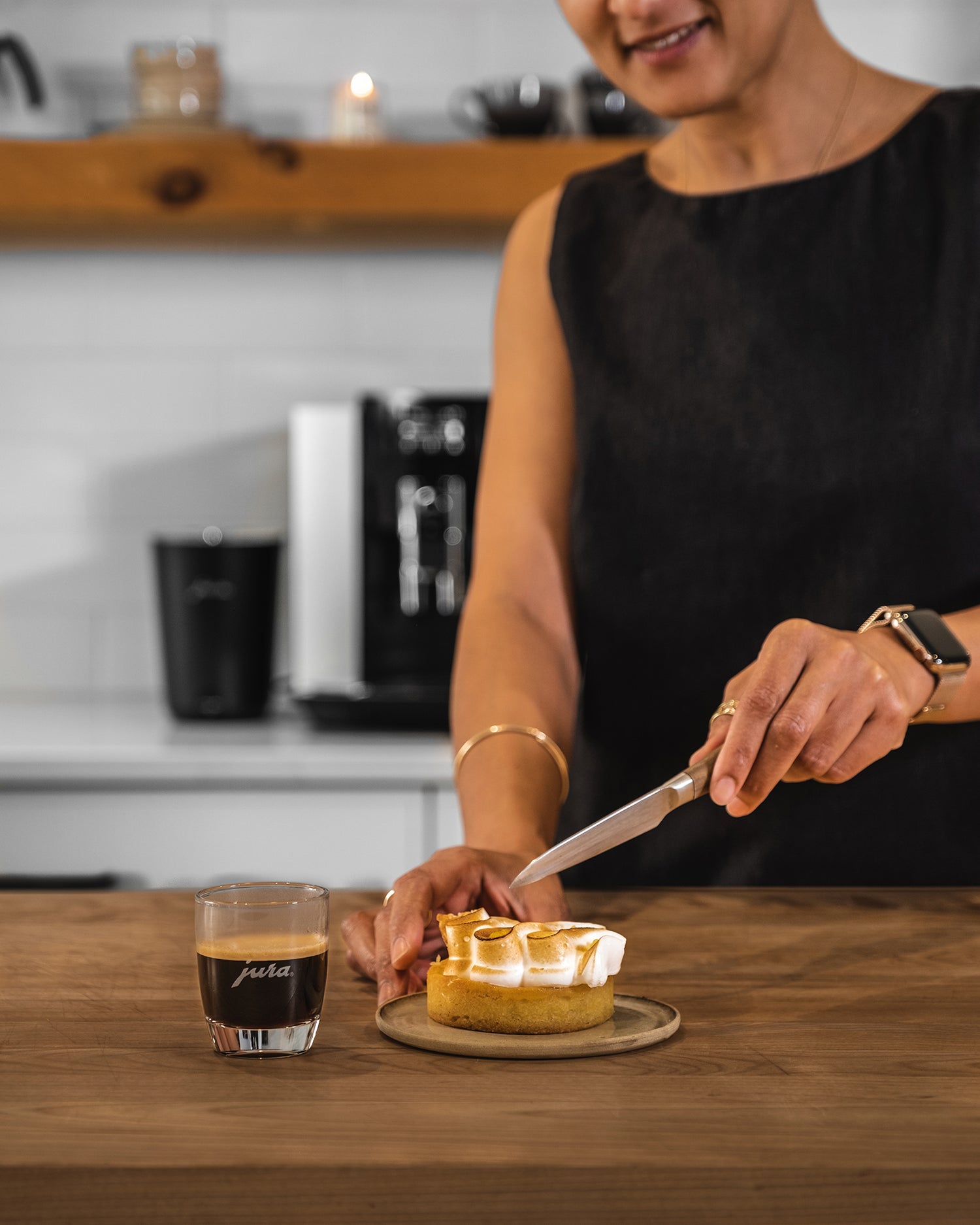 Femme coupant une pâtisserie à côté d'une tasse d'espresso JURA. JURA E6 en arrière - plan